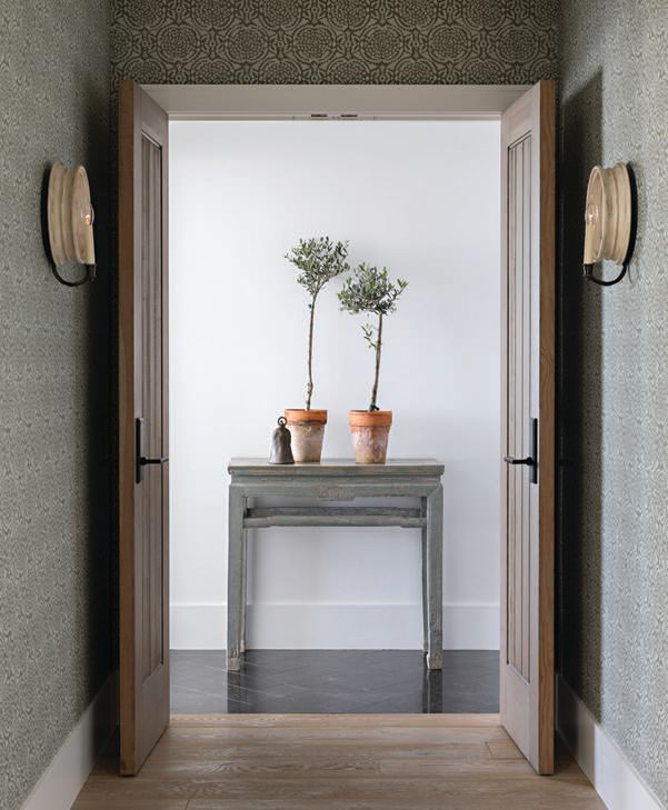 The primary bedroom vestibule is papered in a custom block print by Galbraith & Paul. Th e primary bath table—as seen through the hallway—is vintage. PHOTOGRAPHED BY KARYN MILLET